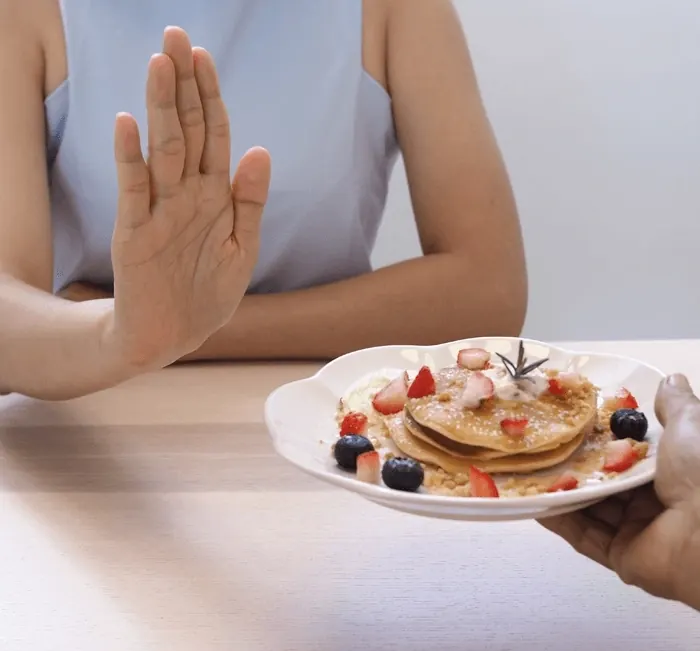 A woman pushing away a plate of pancakes