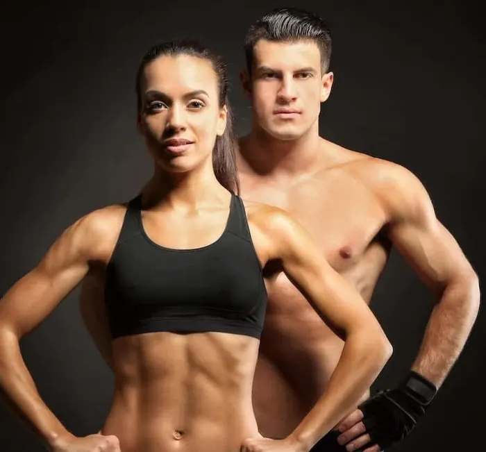 A fit woman and man standing side by side in workout clothes